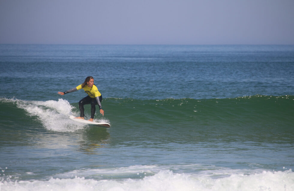 Jeune femme surfant sur une vague, portant un rash guard jaune.