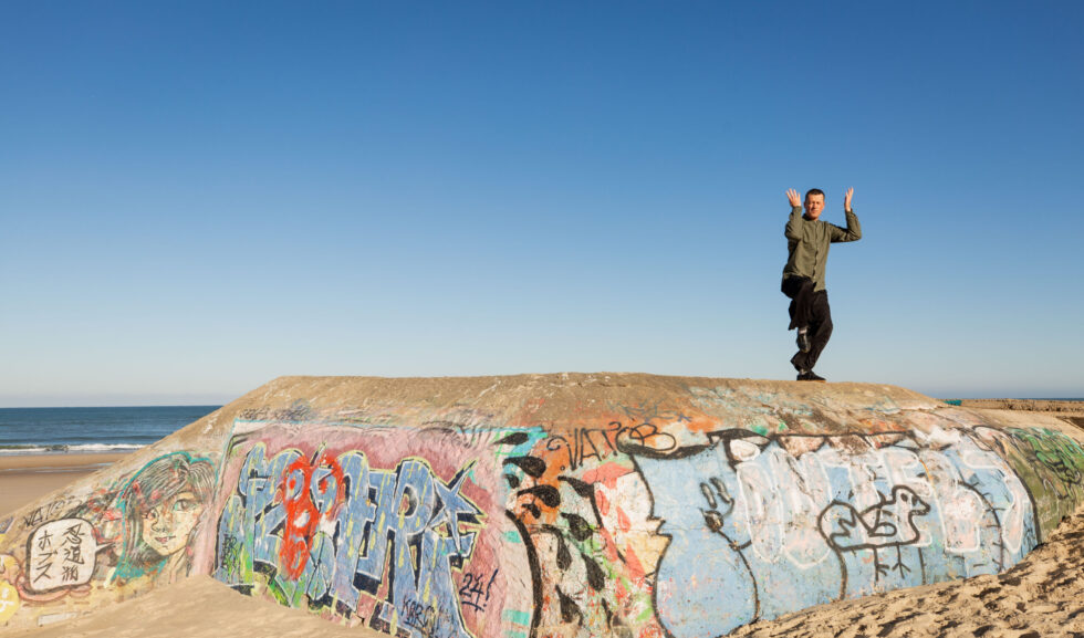 Un homme pratiquant le Tai Chi sur un mur couvert de graffitis sur la plage.