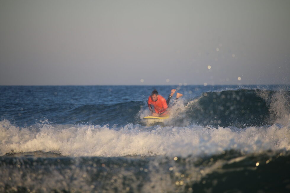 Un surfeur en rashguard orange s'effondre sur une vague.