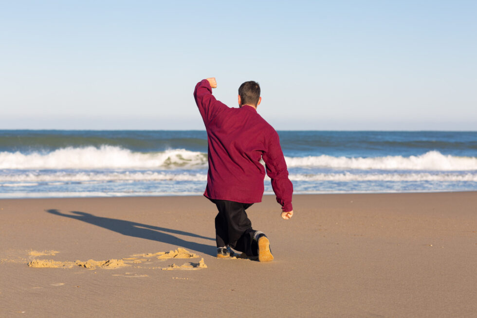 Homme pratiquant les arts martiaux sur une plage, face à l'océan.