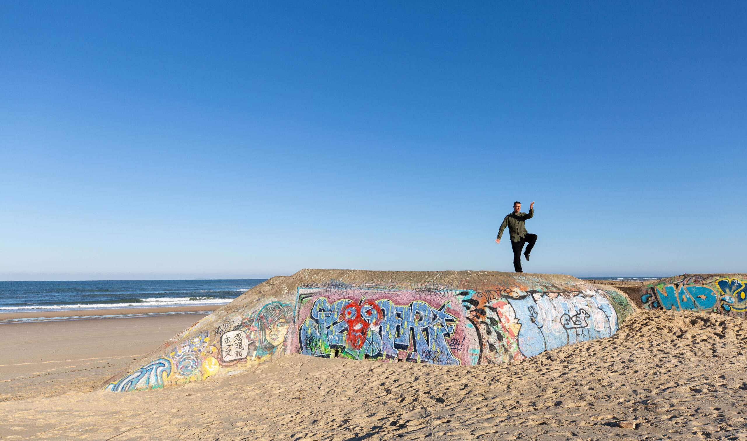 Un homme pratiquant le Tai Chi sur un bunker de plage couvert de graffitis