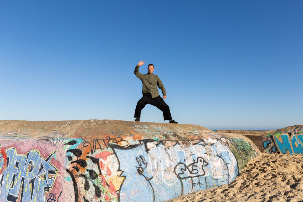 Un homme pratiquant le Tai Chi sur un mur couvert de graffitis au bord de l'océan.