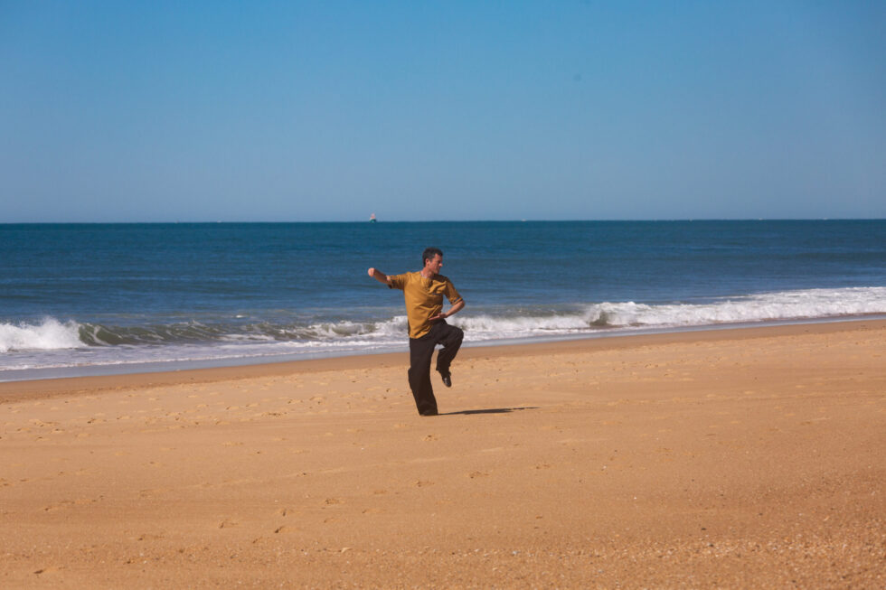 Un homme pratiquant le Tai Chi Chuan sur une plage de sable.
