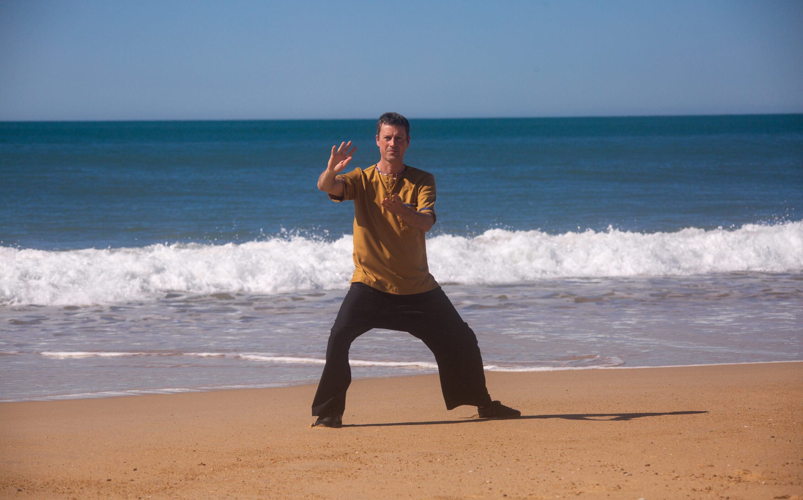 Un homme pratiquant le Tai Chi Chuan sur une plage