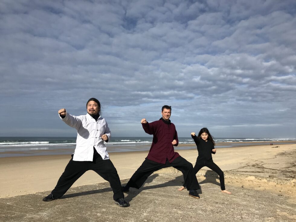 Trois personnes pratiquant des arts martiaux sur une plage