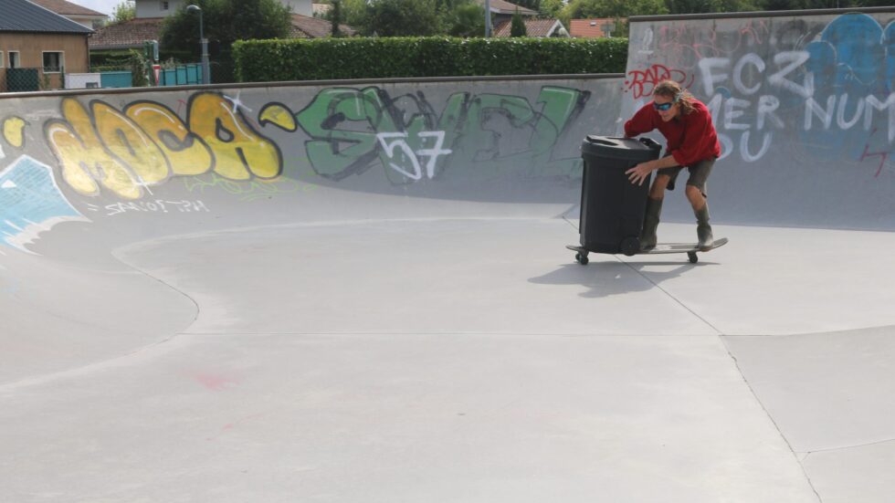 Un homme fait du skateboard avec une grande poubelle dans un skatepark.