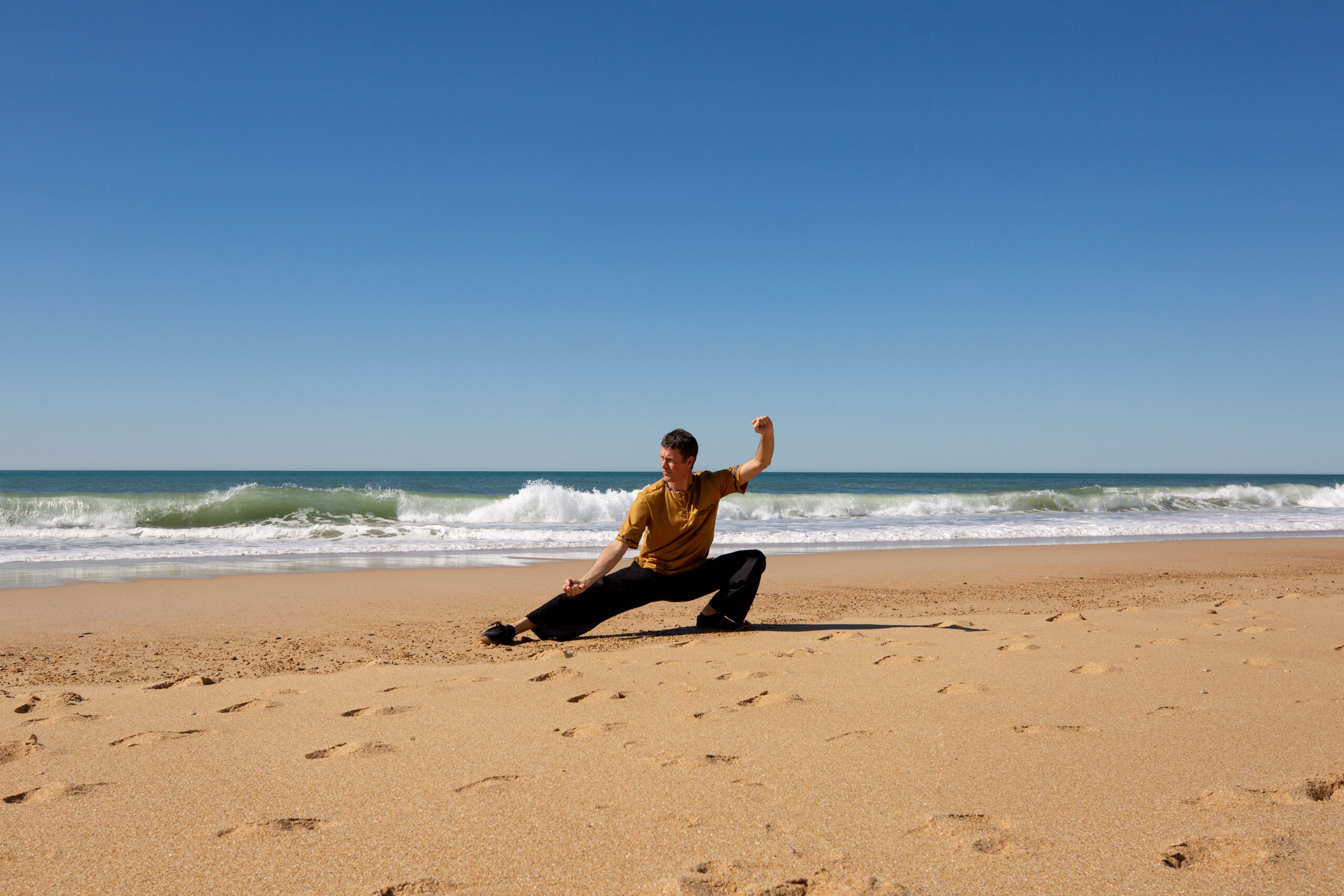 Un homme pratiquant le Tai Chi Chuan sur une plage de sable