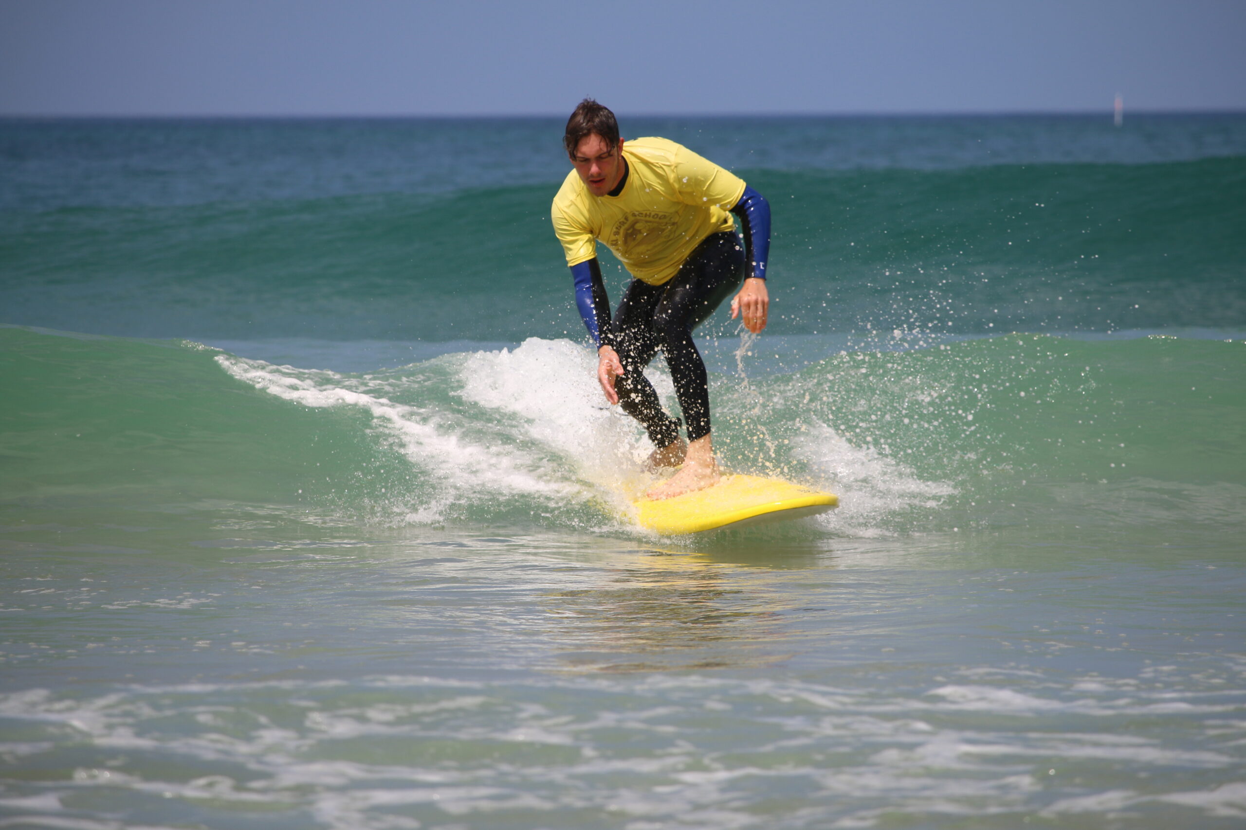 Surfeur en combinaison jaune surfant sur une vague verte sur une planche jaune.