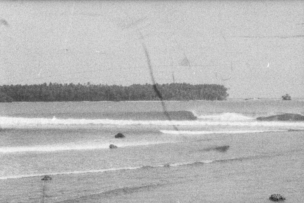 Vague, grainy image of waves breaking on a tropical beach with palm trees in the background.
